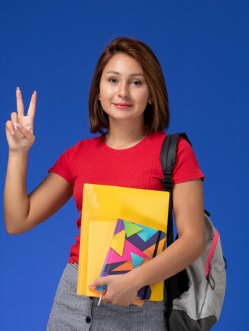 front-view-young-female-student-red-shirt-wearing-backpack-holding-files-copybook-posing-blue-background (1)